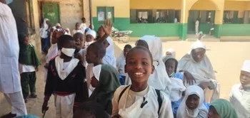 children in the school yard waving at the camera